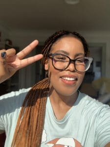 profile pic 1 Profile photo of Amanda, a Black woman with ginger braids, black eyeglasses, and blue tshirt, right hand in a peace sign and smiling