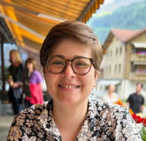 EUR2023-0483_Original A white woman in her late 20s with short brown hair and round glasses wearing a black-and-white floral men's button-up.