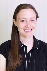 Maggie Cooper-small a thirty-something white woman with freckles and long brown hair over one shoulder, in a collared black and white shirt